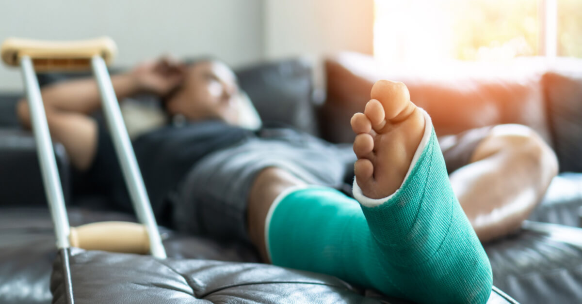 Bone fracture foot and leg on male patient with splint cast and crutches during surgery rehabilitation and orthopaedic recovery lying on couch staying at home