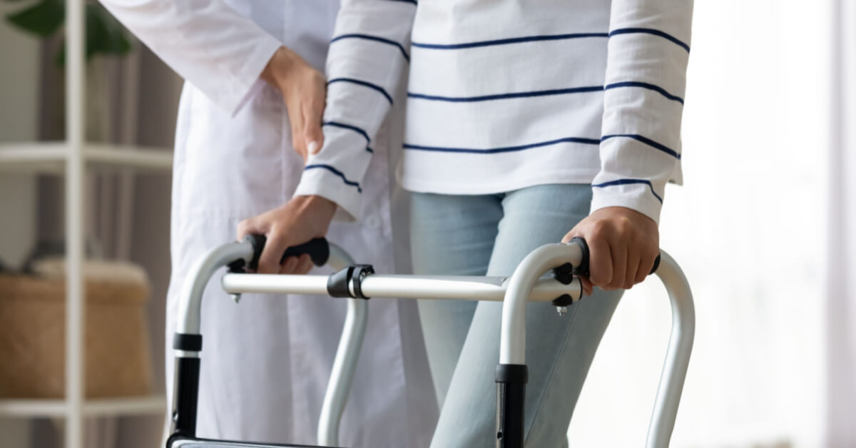 Cropped image caregiver helping to disabled patient walking with rollator equipment reduce load and joint pain with arthritis. Physical therapist and therapy, neurological cerebellar disorders concept