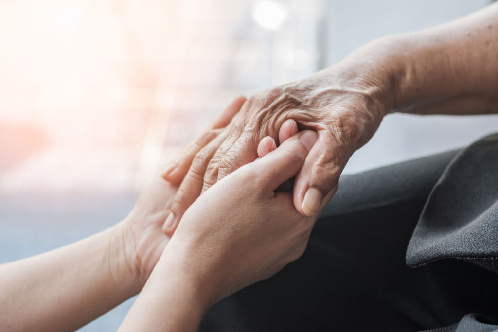 Arthritis person's hand in support of nursing family caregiver care for disability