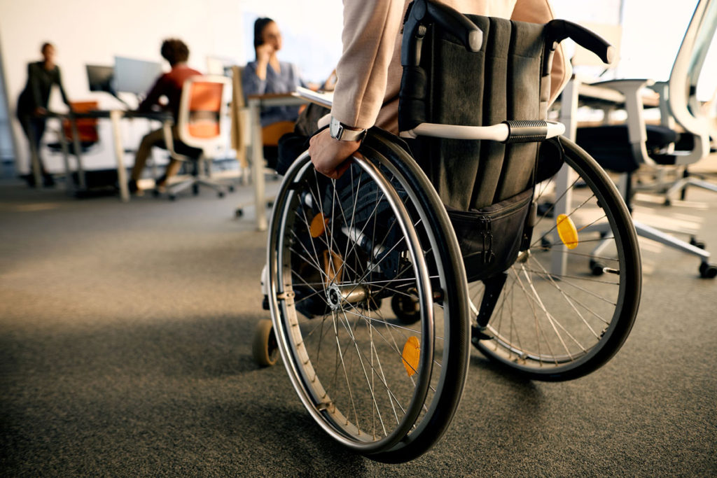 Rear view of businesswoman with disability uses wheelchair while going through the office.